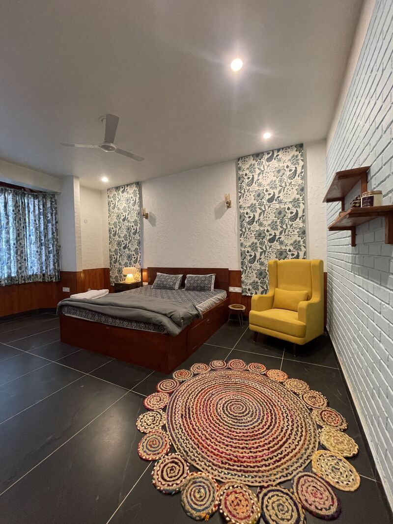 The Mehal room, with floral panel wallpaper, a wooden bed and a yellow reading chair